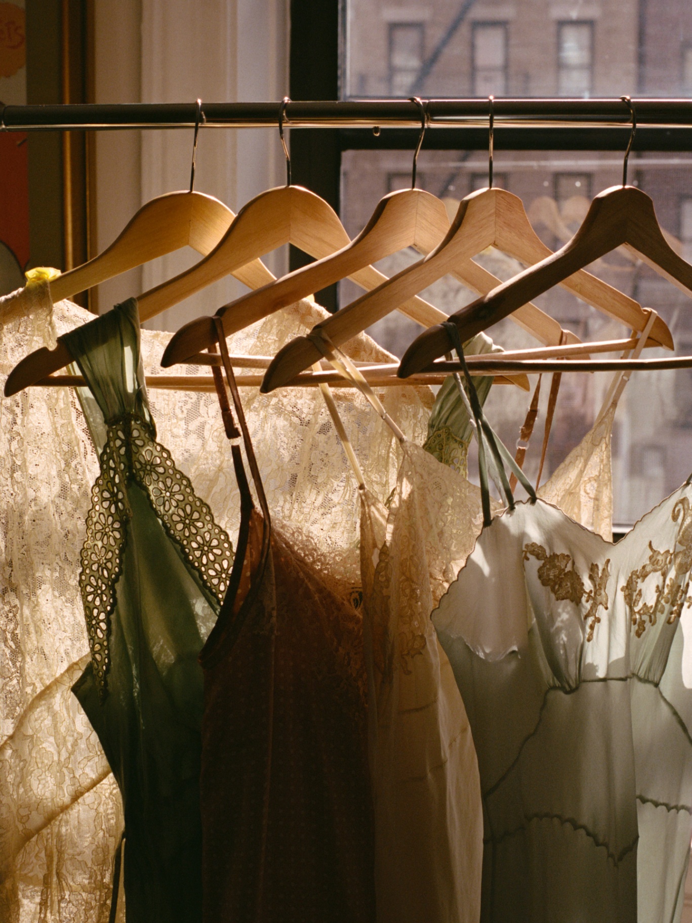 A curated closet rail with three considered neutral coats in soft window light